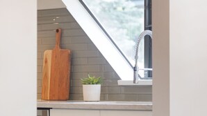 A kitchen with white cabinets, a wooden cutting board, a potted plant, and a window above the sink. - Luxury 3BR/2BA-1700 sq ft, Mountain view,BBQ (Whistler)