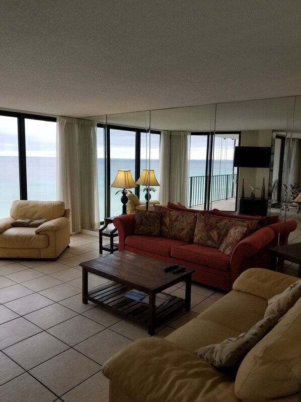 A spacious living room with a large window overlooking the sea, a beige sofa, a red sofa, and a coffee table.