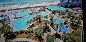 An aerial view of a resort with multiple swimming pools, palm trees, and a beach area.