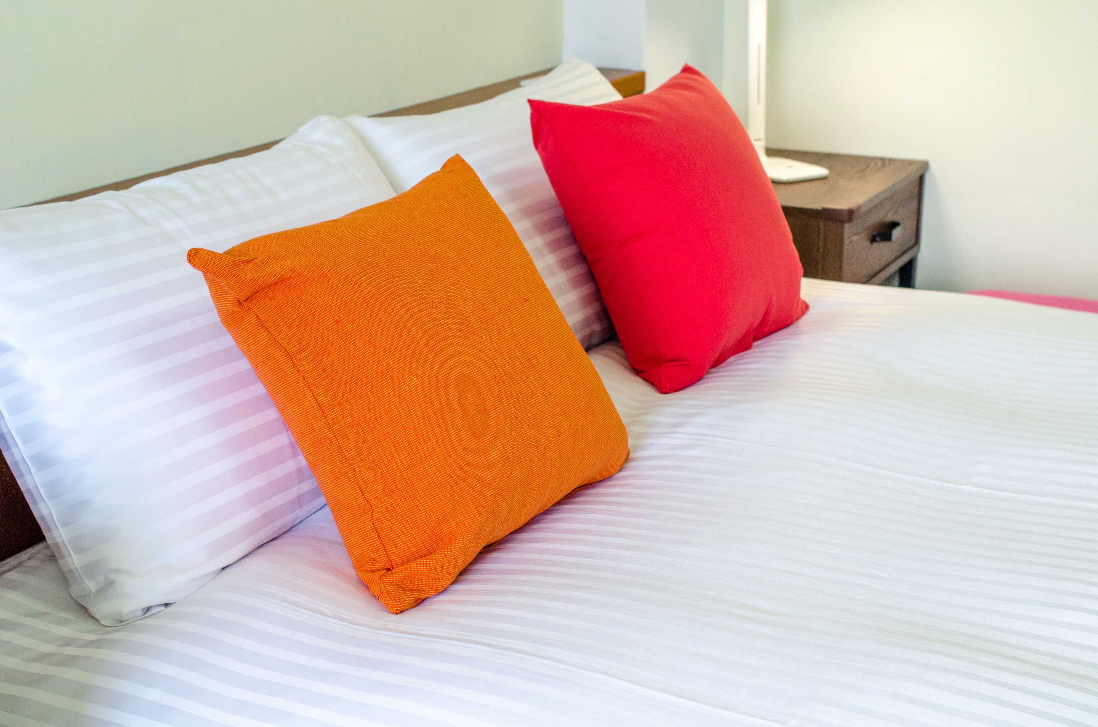 A bed with white and orange pillows and a red pillow.