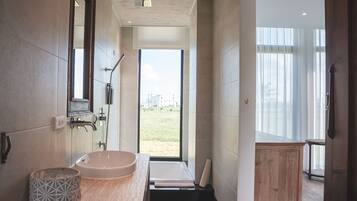 Un baño moderno con una bañera grande, un lavamanos y zona de ducha. Se ve un campo cubierto de césped a través de un ventanal.