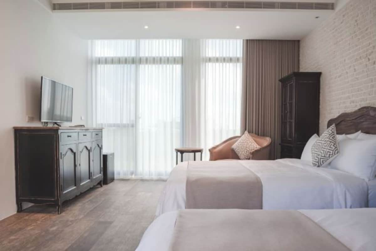Una habitación de hotel con una cama, televisión, armario y ventana con cortinas.