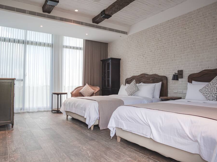 A hotel room with two beds, a wooden cabinet, and a large window with curtains.