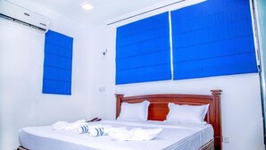 Ein ordentlich bezogenes Bett mit weißen Leinen und Kissen, ein Holz-Kopfteil und blaue Fensterläden an den Wänden.