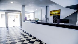 Ein Empfangsbereich mit Schachbrettmuster-Boden, einer Rezeption, einem Bild an der Wand und einer Treppe.