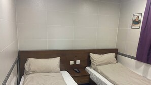 Ein Doppelzimmer mit zwei Einzelbetten, einem Holz-Kopfteil, einem kleinen Nachttisch und einem an der Wand montierten Lichtschalter.