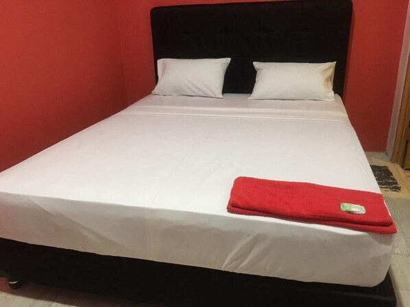 A single bed with white bedding and a red blanket, set against a red wall. - Coconut Hotel - Hostel (Kediri)