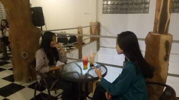 Duas pessoas sentadas numa mesa redonda com bebidas, num espaço com chão quadriculado e pilares de madeira.