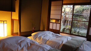Een traditionele Japanse kamer met twee bedden, een houten vloer en uitzicht op een tuin door een schuifdeur.