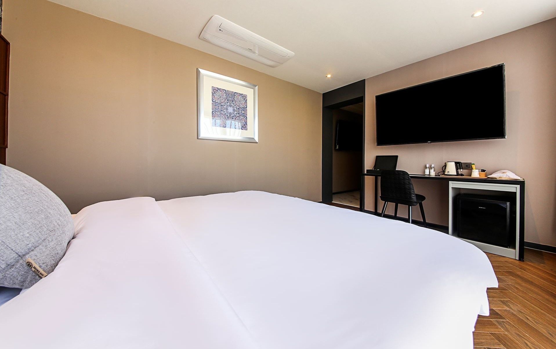 Une chambre d’hôtel comprenant un lit, un bureau avec une chaise, un téléviseur à écran plat et un tableau encadré au mur.