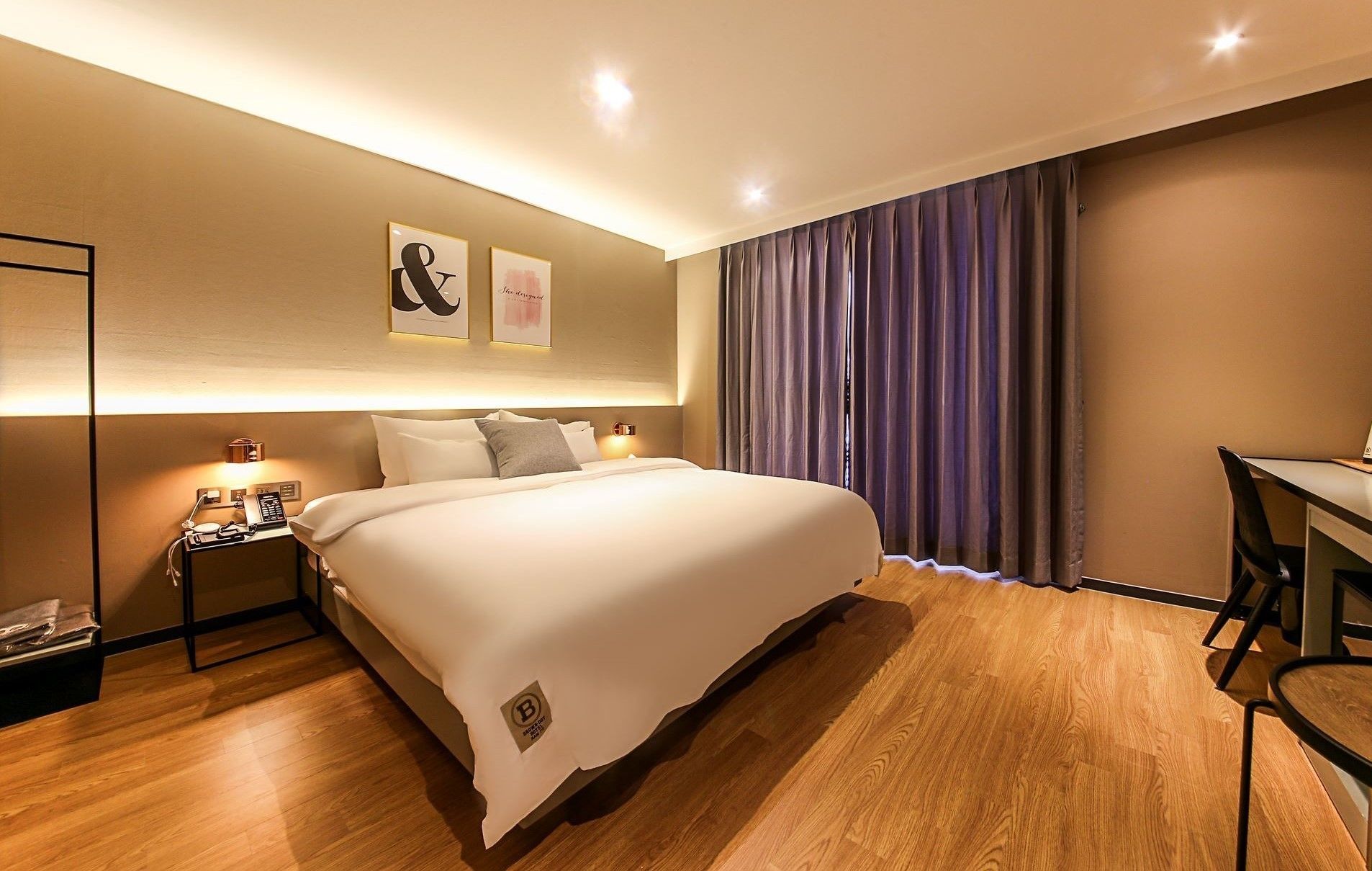 Habitación de hotel con una cama grande, mesitas de noche, un escritorio y vistas a la ciudad a través de cortinas.