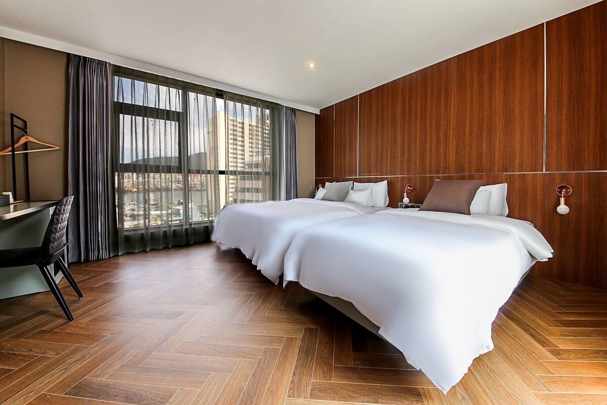Een hotelkamer met een groot bed, een bureau en uitzicht op de stad door grote ramen.