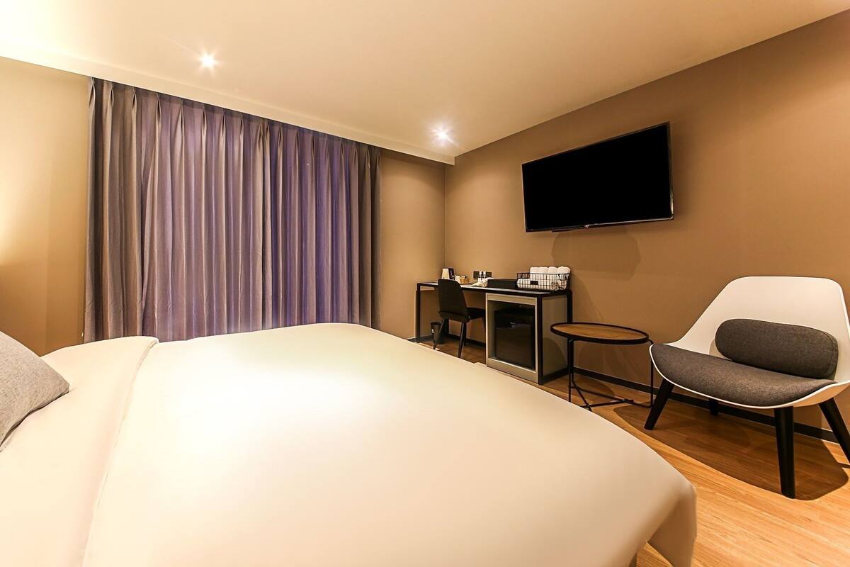 Een hotelkamer met een bed, een bureau, een stoel, een televisie en een raam met gordijnen.