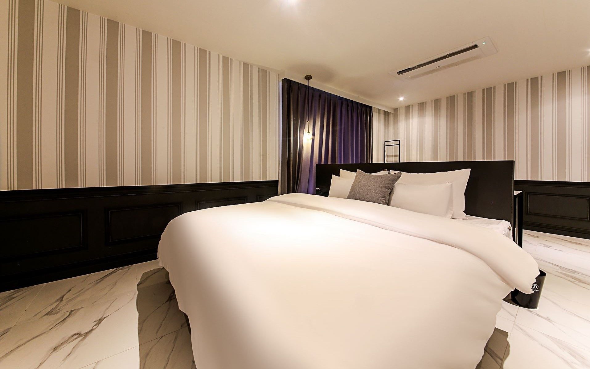 A modern hotel room with a large bed, striped wallpaper, and a dark headboard.
