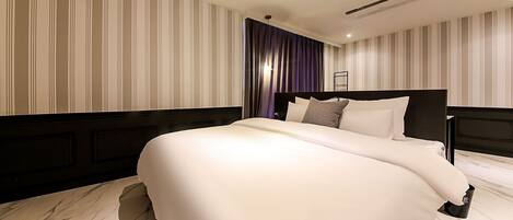 A modern hotel room with a large bed, striped wallpaper, and a dark headboard.