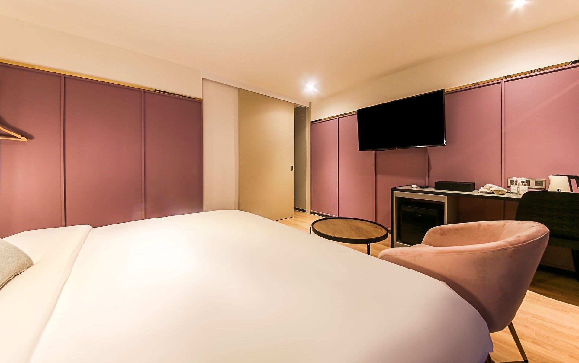 Habitación de hotel moderna con una cama grande, un escritorio con televisor de pantalla plana y una silla rosa.