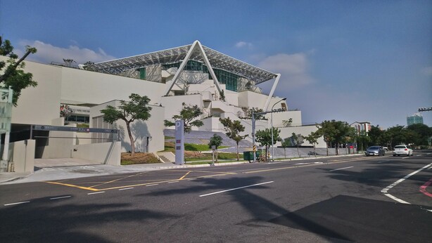 A modern building with a unique triangular roof structure, a parking area with marked spaces, and a clear sky. - Jia Inn (Tainan)