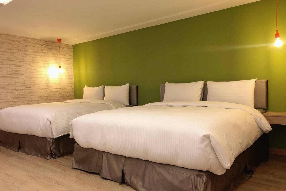 Habitación de hotel con dos camas, paredes verdes y suelo de madera.