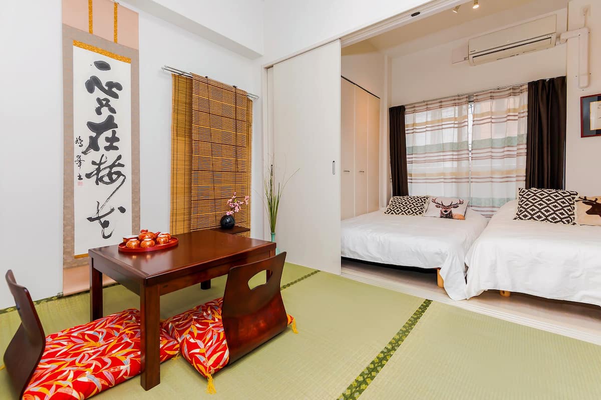 Ein Hotelzimmer im traditionellen japanischen Stil mit Tatami-Böden, einem niedrigen Holztisch und einem Bett mit gemusterten Kissen.