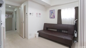 A modern living room with a brown sofa, a vacuum cleaner, and a window with curtains. - 7mins Shinsaibashi Comfortable Apartment (Osaka)