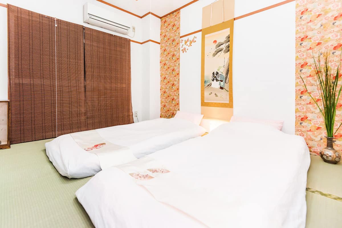 A hotel room with two beds, a traditional Japanese shoji screen, a wall with floral wallpaper, and a painting of a landscape.