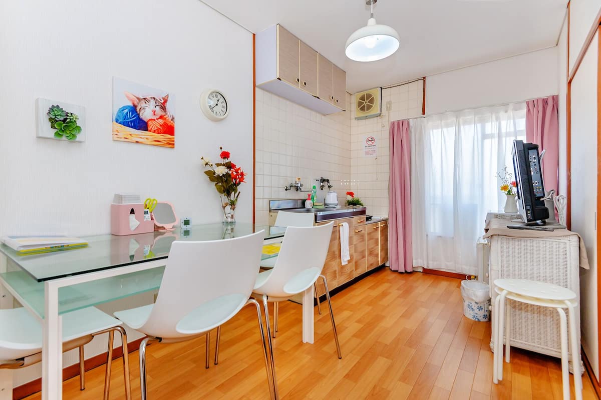 A modern kitchen with white cabinets, a glass dining table, and white chairs. There is a clock on the wall and a small plant on the counter.