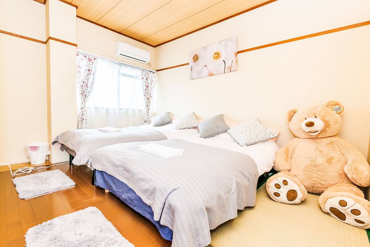 A bedroom with two beds, a large teddy bear, and a painting on the wall.