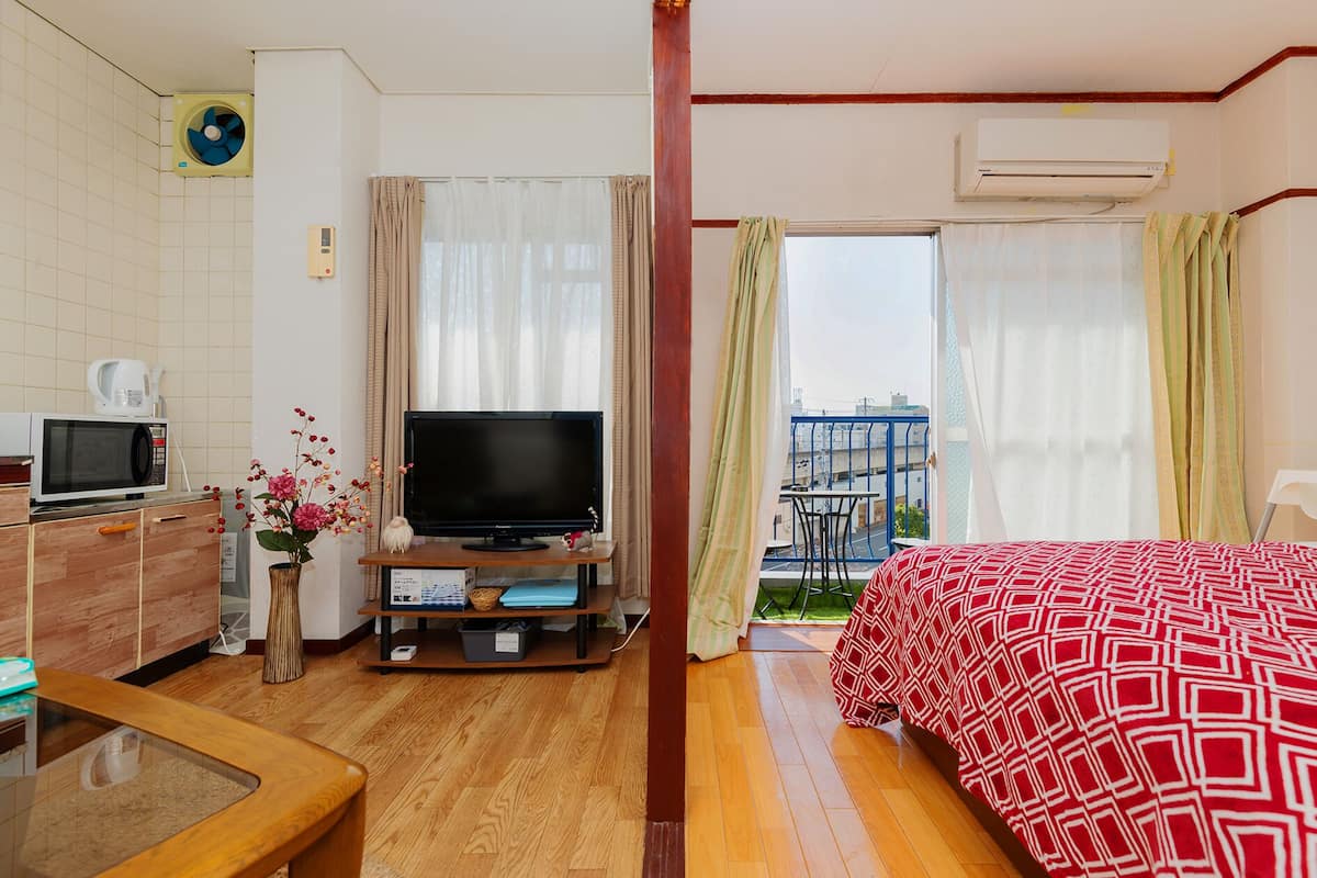 A hotel room with a bed, a TV, a microwave, a small table, and a balcony with curtains.