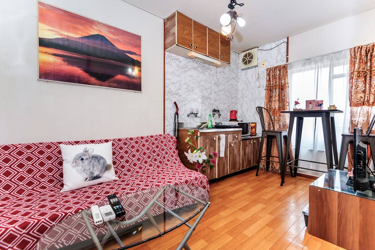 A living room with a sofa, a glass coffee table, and a kitchen area with a sink and cabinets.