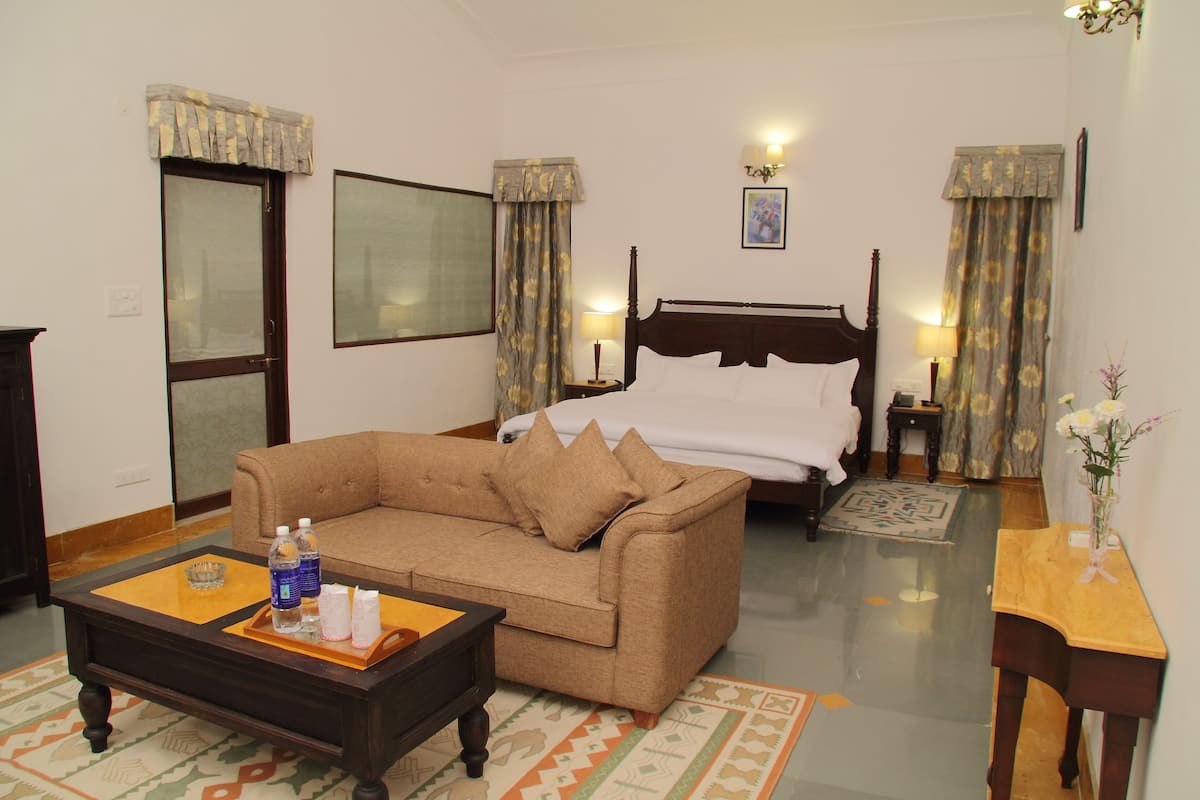 Quarto de hotel com cama, sofá, mesa de centro e pequena mesa com um vaso.