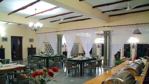 A dining area with tables and chairs, a chandelier, and a row of covered buffet stations. - Jhadol Safari Resort (Jharol)
