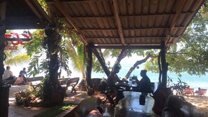 Un espacio de estar al aire libre con techo de madera, rodeado de palmeras y vistas a la playa.