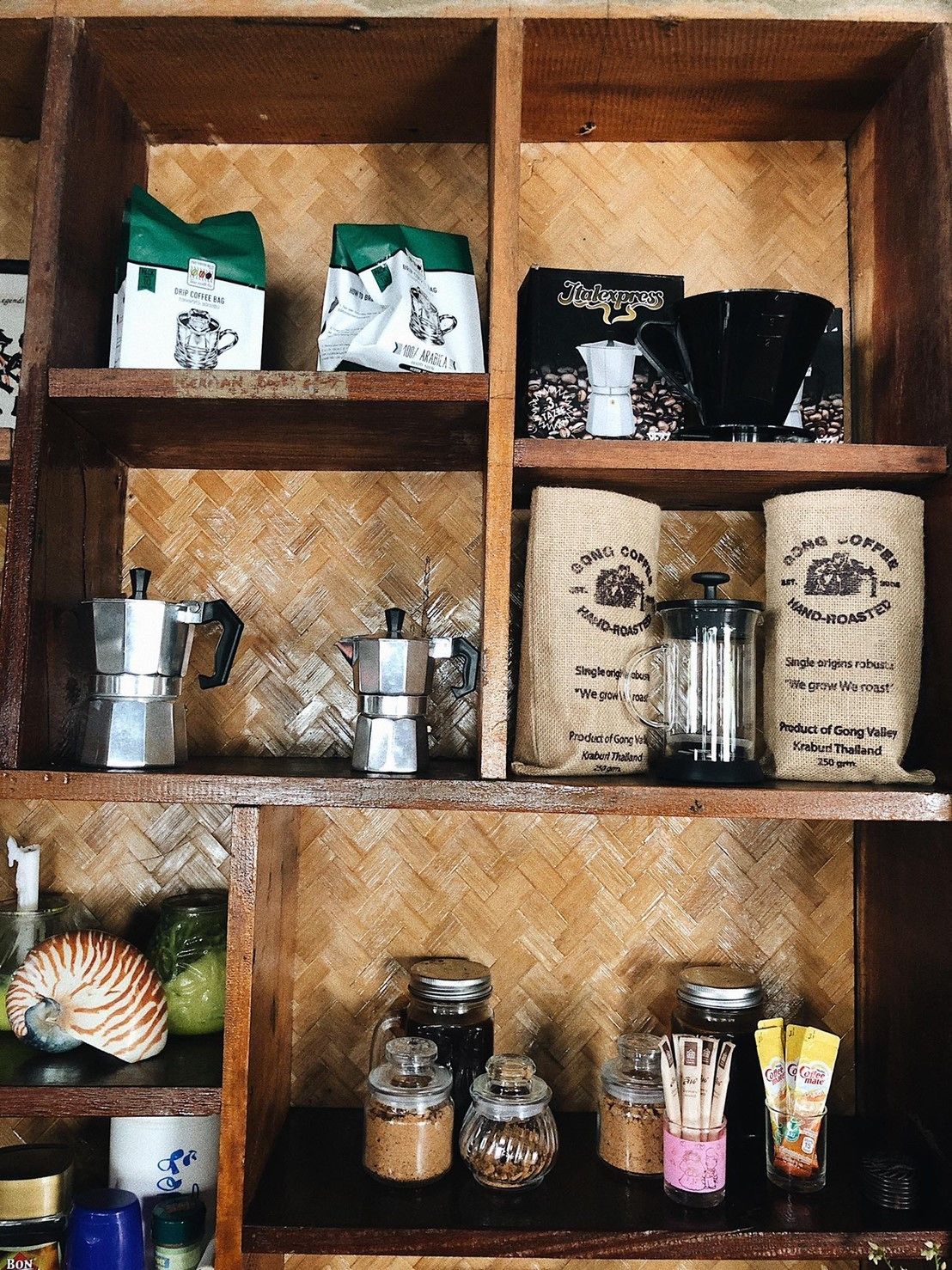 A wooden shelf with various coffee-related items, including bags, a moka pot, and jars.