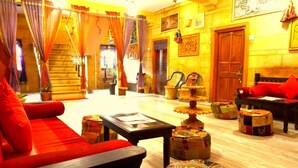 A traditional room with a sofa, a table, and a chair. There are decorative items and a door in the background. - Prithvi Palace (Jaisalmer)