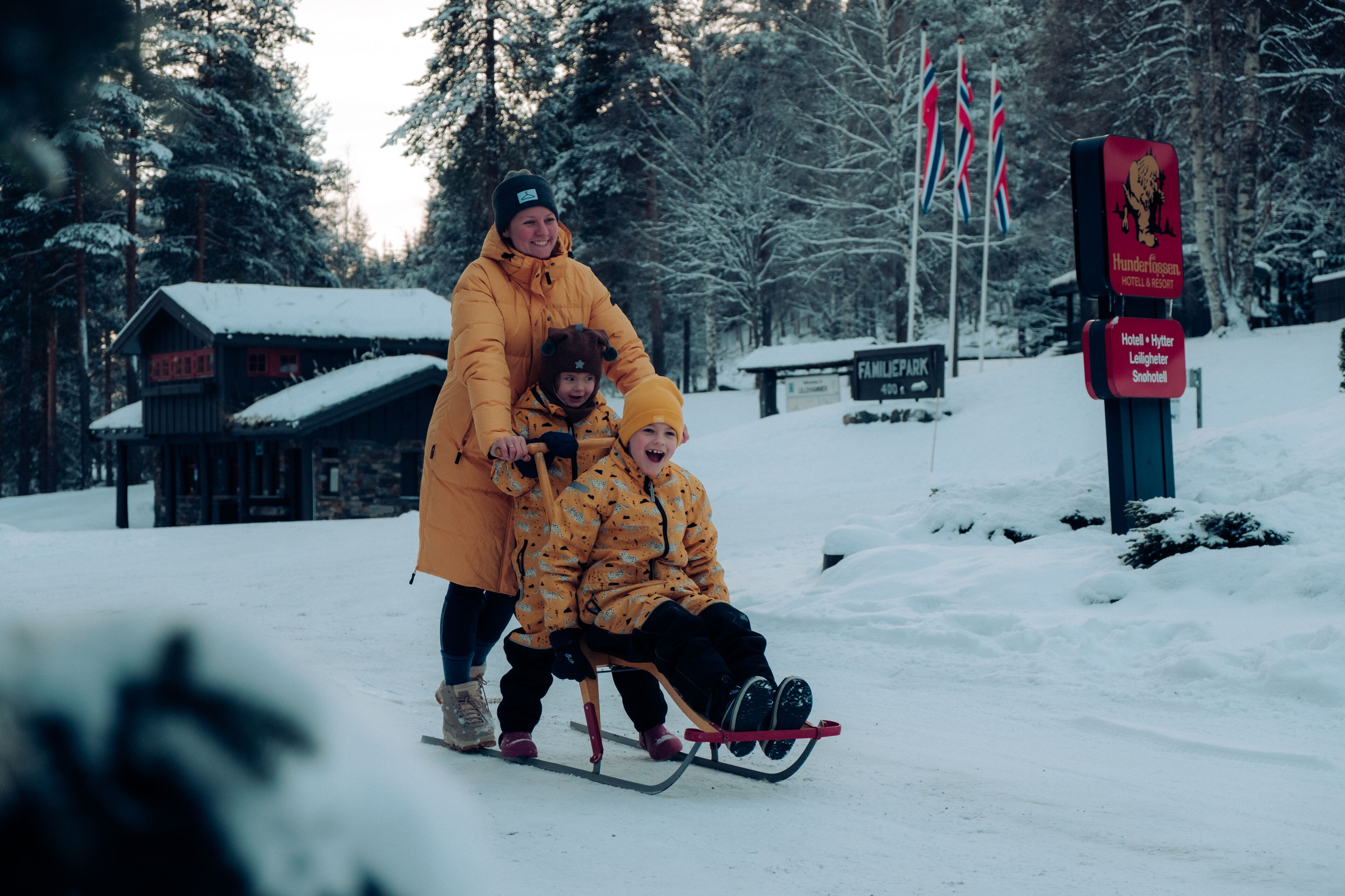 Et snøklædt udendørs område med en slæde, en træhytte og et skilt til et hotel.
