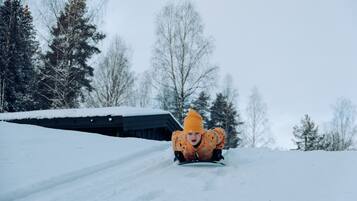 A child sledding down a snowy slope with a house in the background.