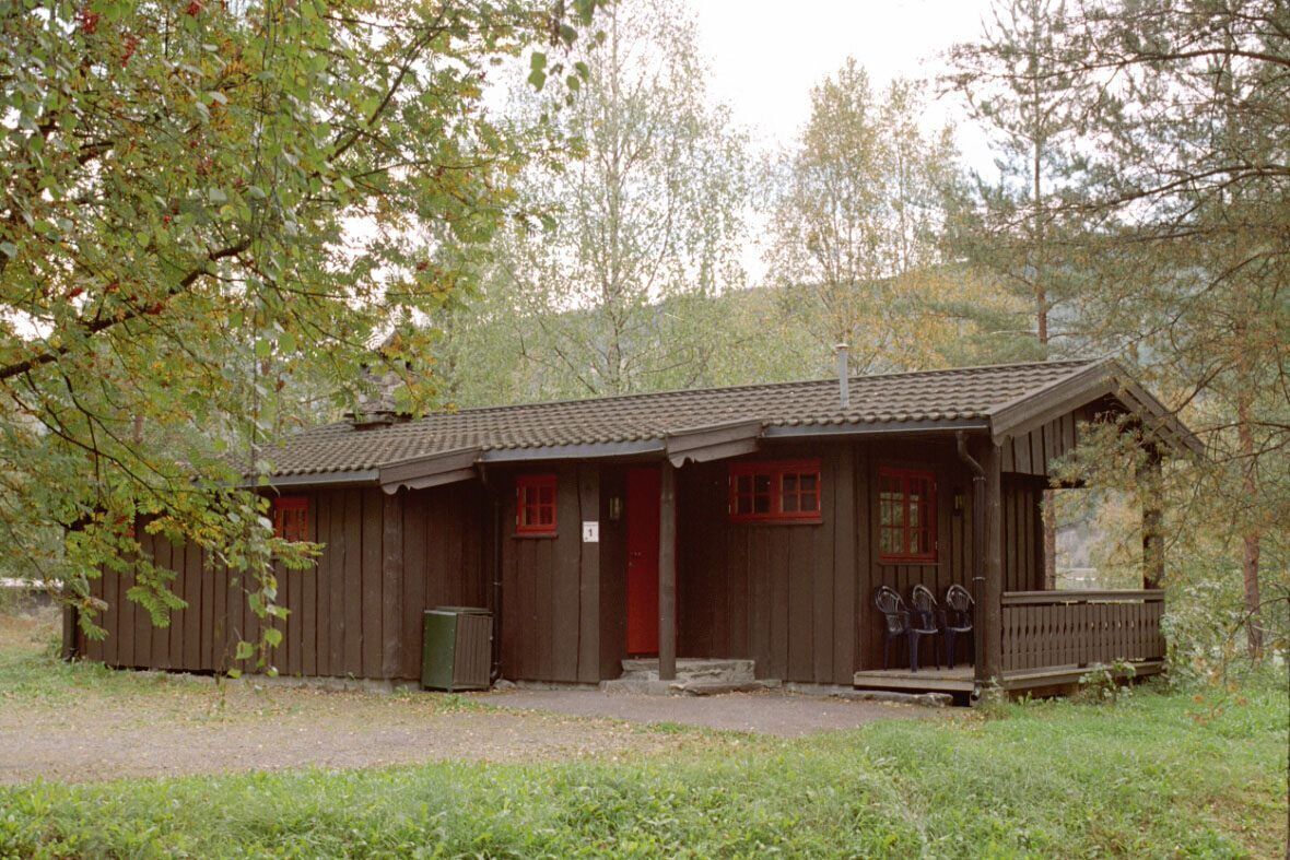 A rustic wooden cabin with a porch and two windows, surrounded by trees.