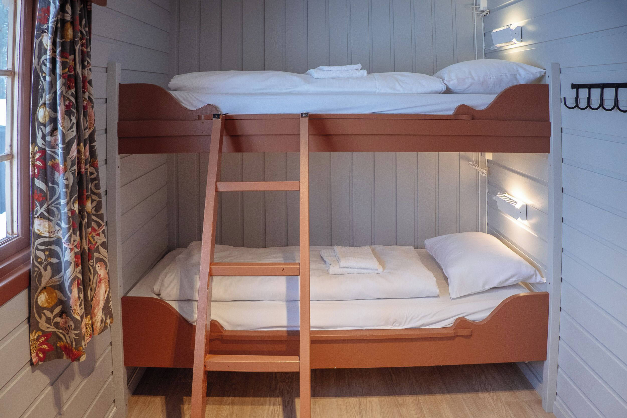 A bunk bed room with a ladder, white bedding, and a curtain with a floral pattern.