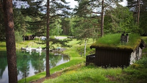 Un cadre paisible au bord d’un lac, avec un cygne sur l’eau, un petit quai et un chalet rustique au toit de chaume.