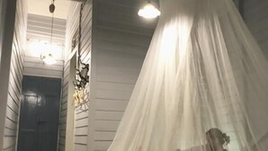 A room with a bed covered by a white canopy, a wooden floor, and a door in the background. - Lhong Yaowarat Hostel (Bangkok)