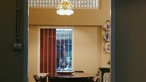 A dining area with a table and chairs, a decorative ceiling, and a window with vertical blinds. - Lhong Yaowarat Hostel (Bangkok)