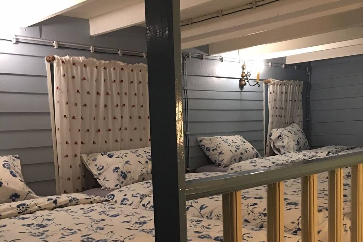 Ett rum med två sängar, där varje säng har sängkläder med blommönster, en sänggavel i trä och ett fönster med gardiner.