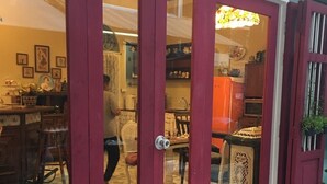 A traditional Chinese restaurant with a red door and glass panels, featuring a tiled floor and various kitchen utensils visible inside. - Lhong Yaowarat Hostel (Bangkok)