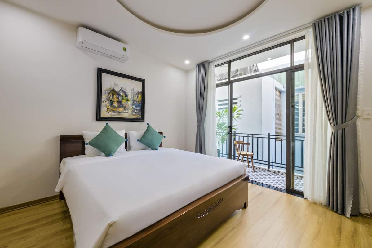 A hotel room with a large bed, a painting on the wall, and a balcony with curtains.
