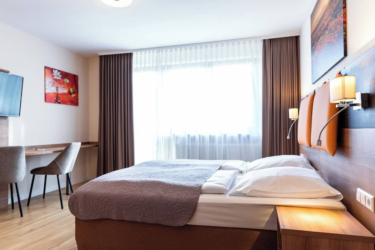 Una habitación de hotel con cama, mesita de noche, lámpara y escritorio con silla.