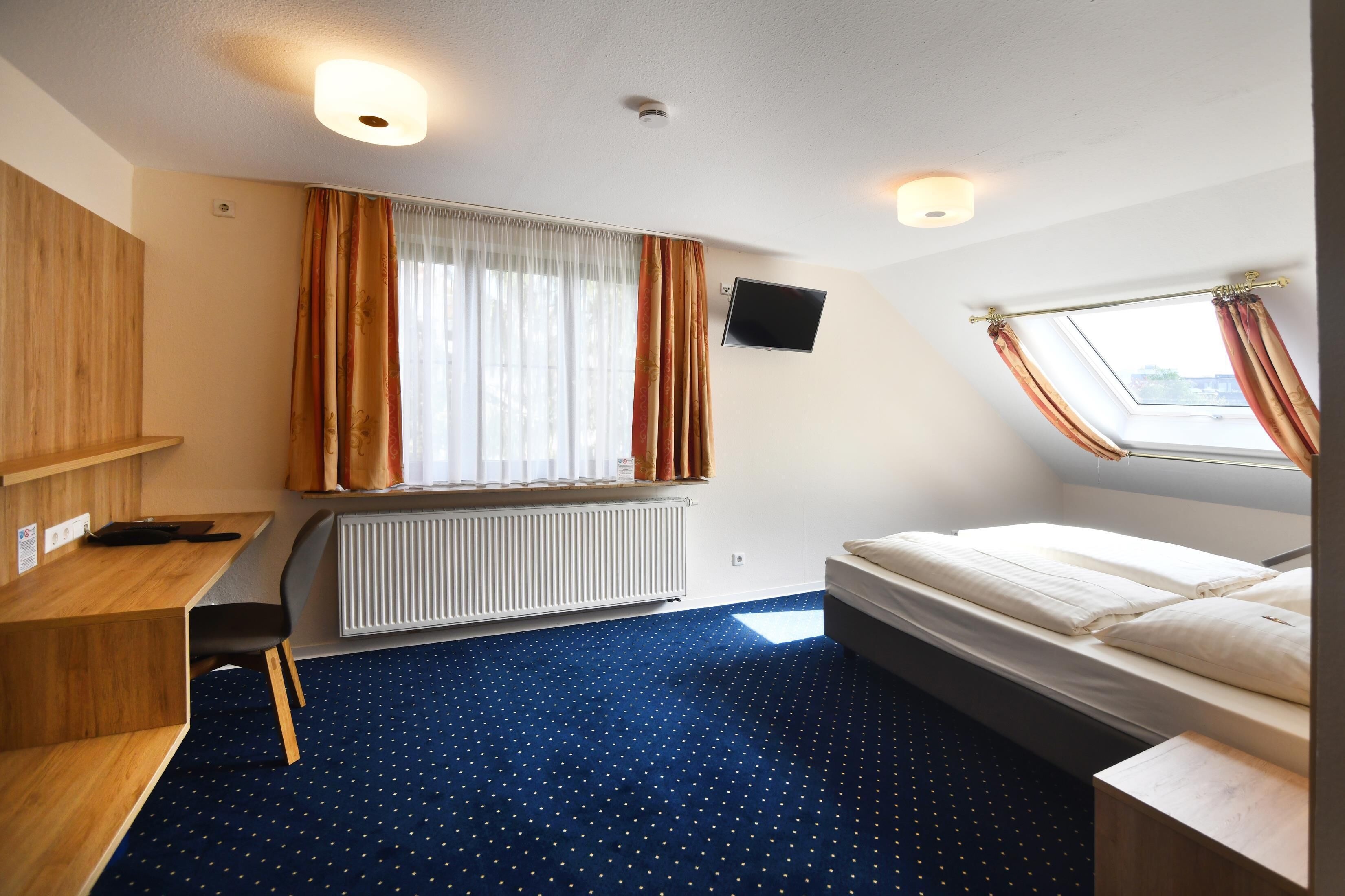 A room with a bed, a desk, a chair, a TV, a window with curtains, and a radiator.