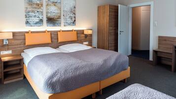 A modern hotel room with a large bed, two bedside tables with lamps, a wardrobe, and a bench.