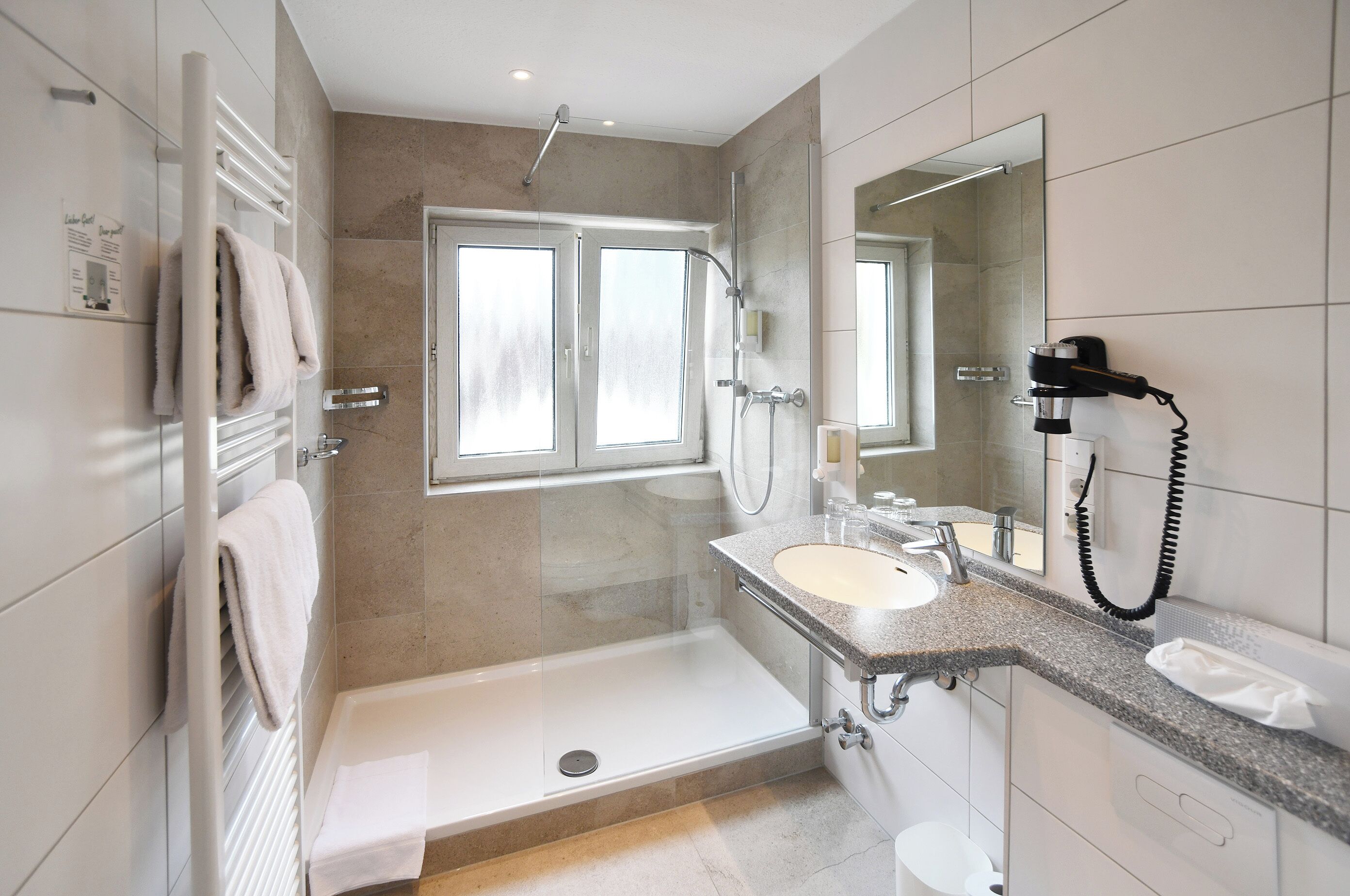 A modern bathroom with a glass-enclosed shower, a built-in sink, and a hairdryer mounted on the wall.