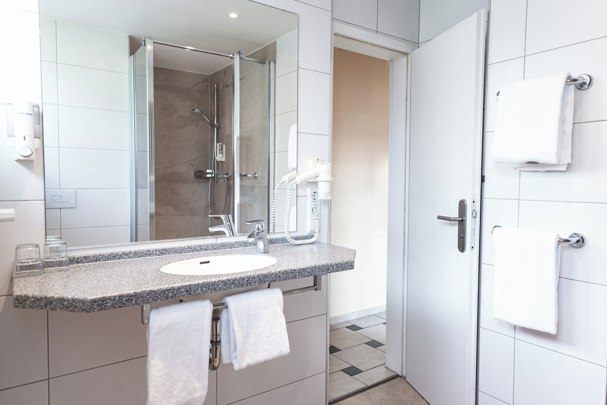 Un baño moderno con lavabo de encimera de granito, un espejo grande, un cabezal de ducha de mano y un perchero.