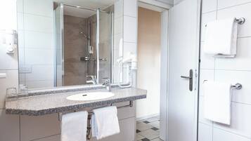 Un baño moderno con lavabo de encimera de granito, un espejo grande, un cabezal de ducha de mano y un perchero.